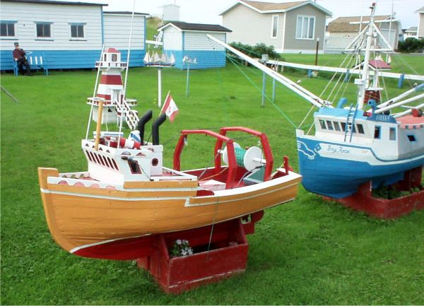 670: A model boat on Lawrence Barry's front lawn in St. Bride's. The boats are large, each  being several feet in length, and are entirely handmade by Mr. Barry. That's him sitting  in front of his workshop at upper left. (2004)